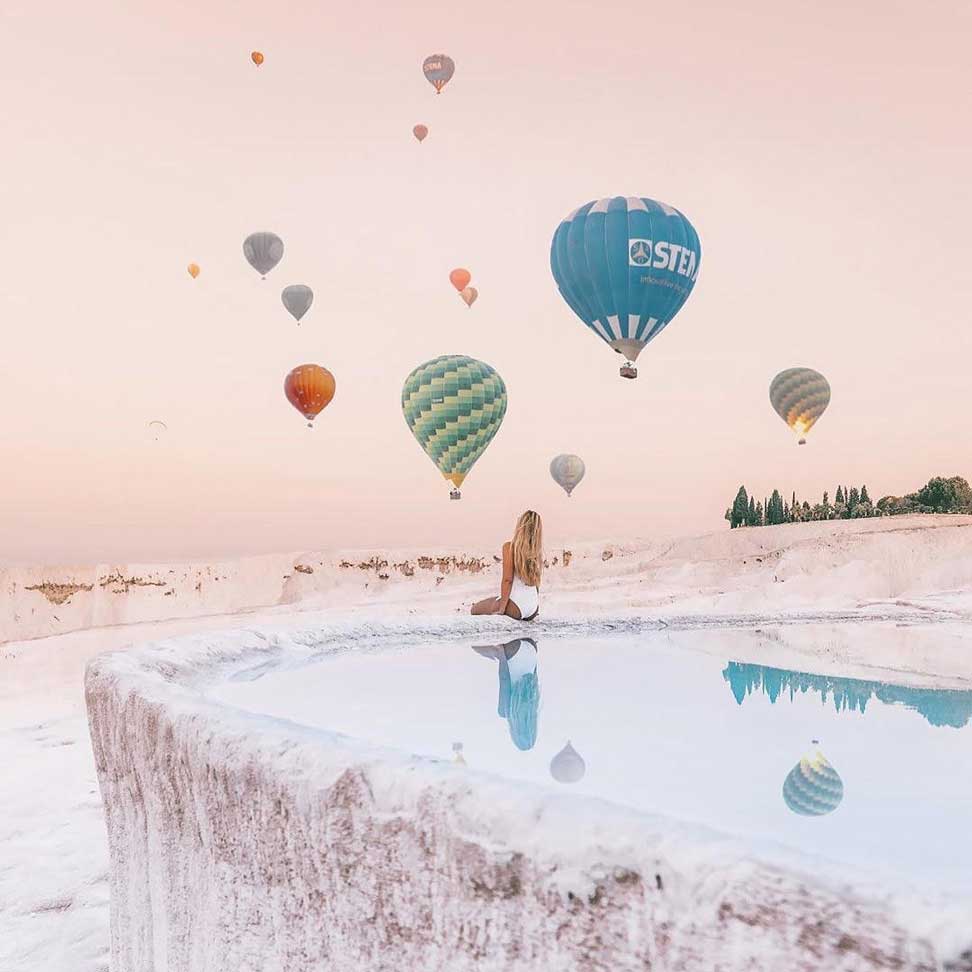 hot air balloons in the sky above Pamukkale pools with a woman looking up
