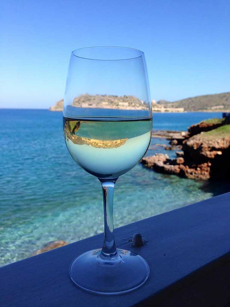 a glas of wine in taverna with Spinalonga island in the distance